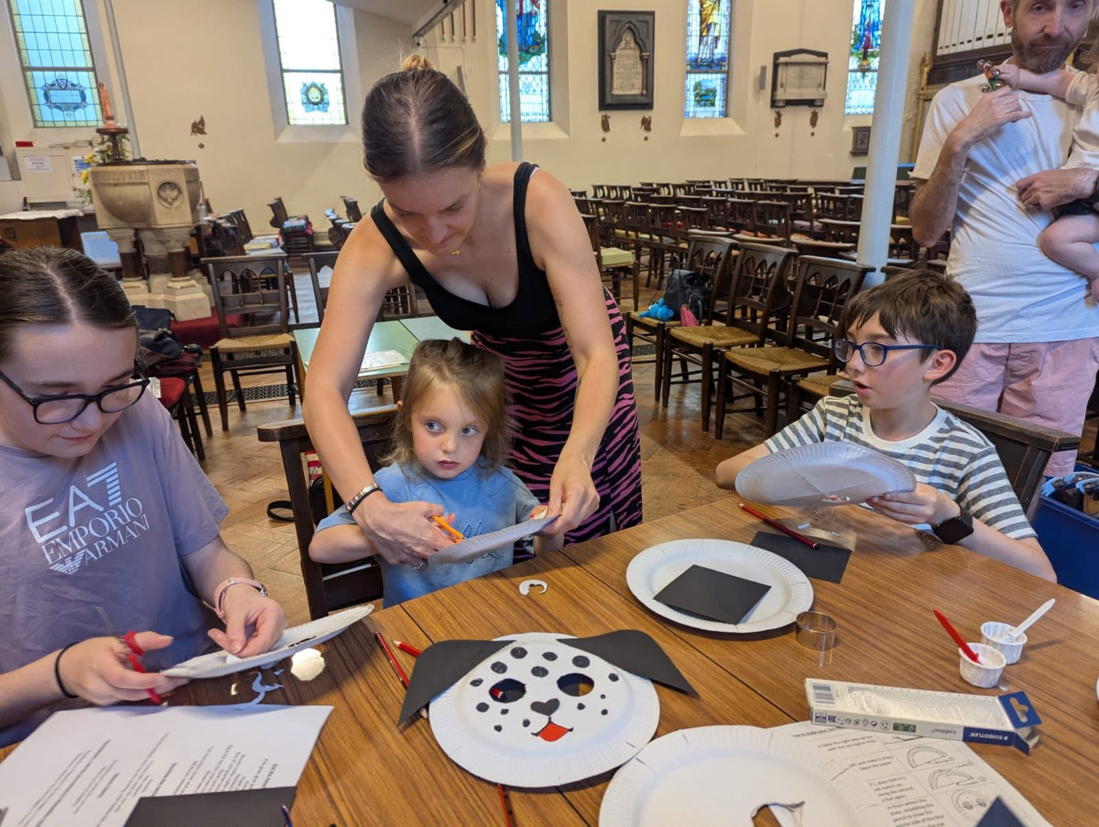 Children sitting around a table doing craft with one being helped by an adult