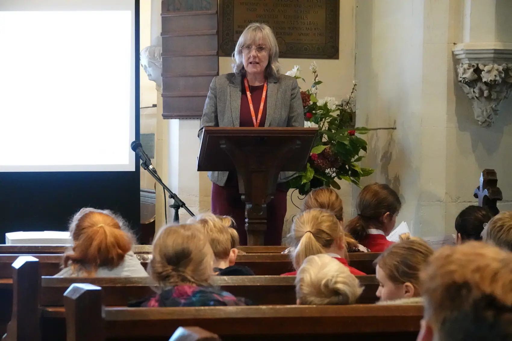The headteacher of Lindridge school stands behind a lectern in church with children sitting in pews in front of her