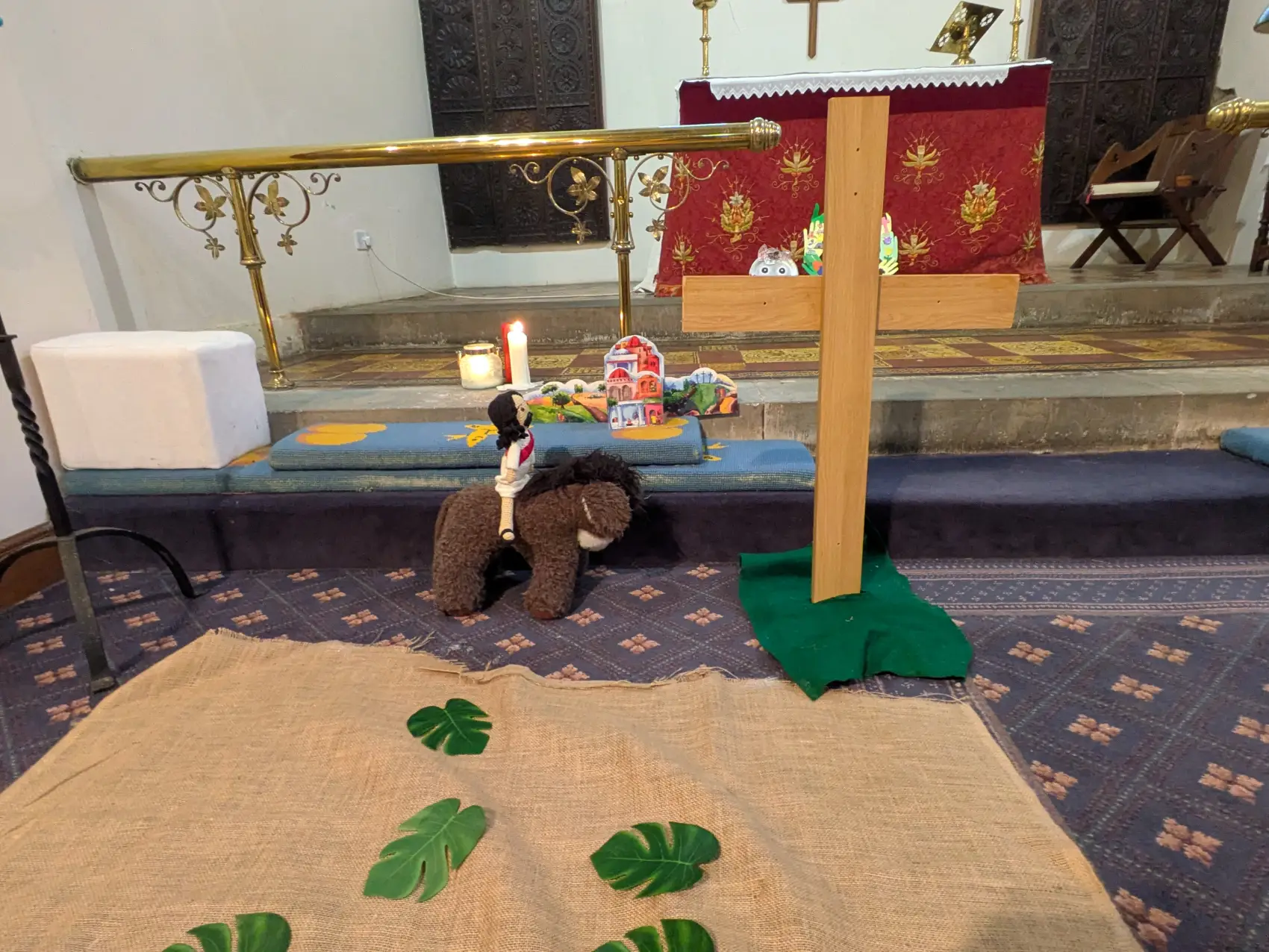 A toy jesus and donkey next to a cross in front of a sack with some palm leaves on.