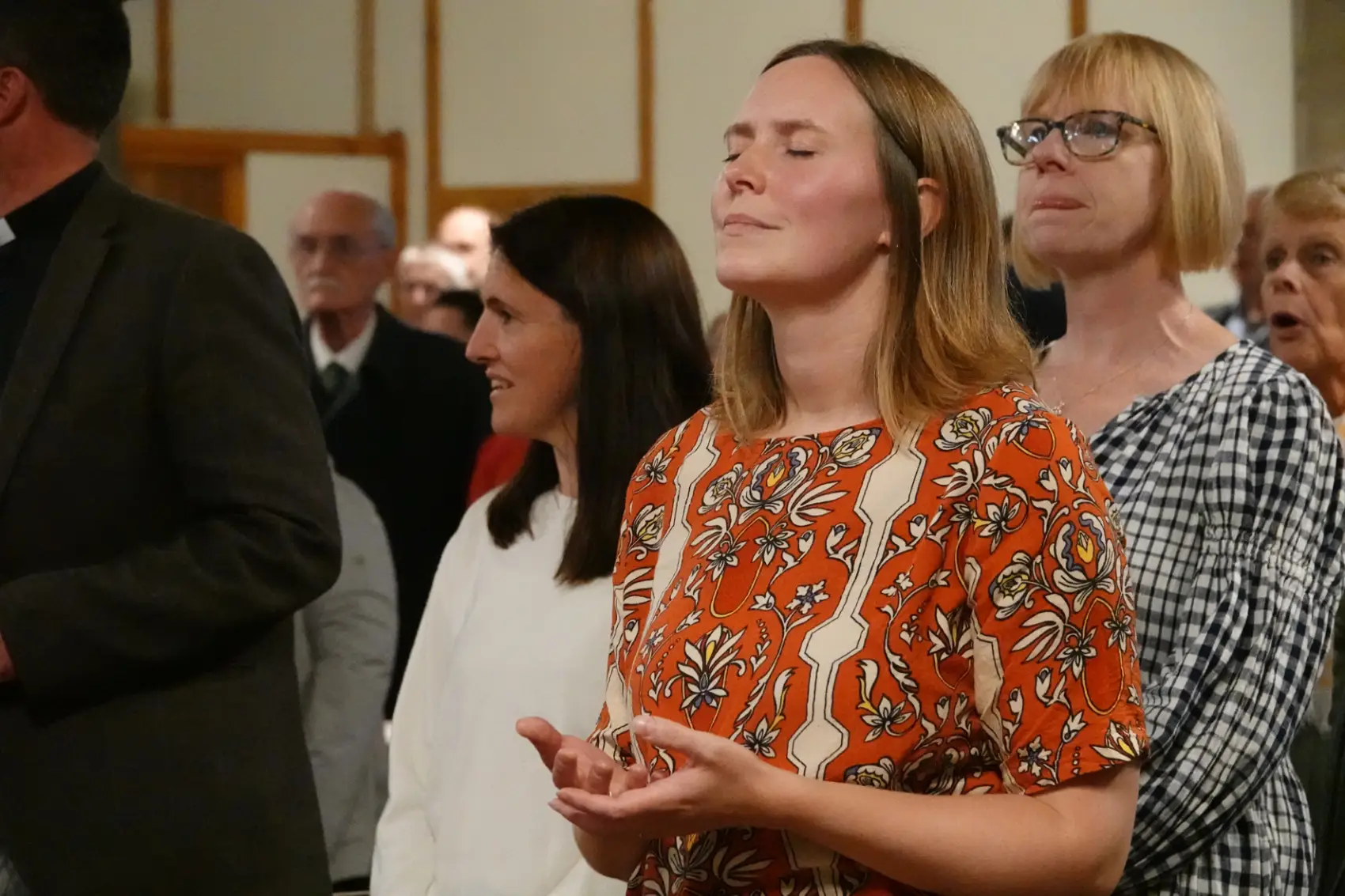 Three women worshipping with the front woman deep in prayer with her eyes closed and hands out.