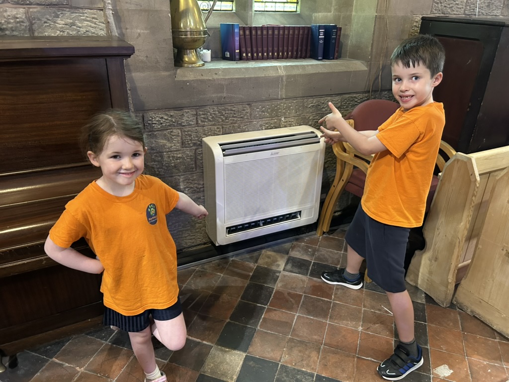 Two children in orange t-shirts pointing at the heater/ air conditioning at St Peter's Cowleigh