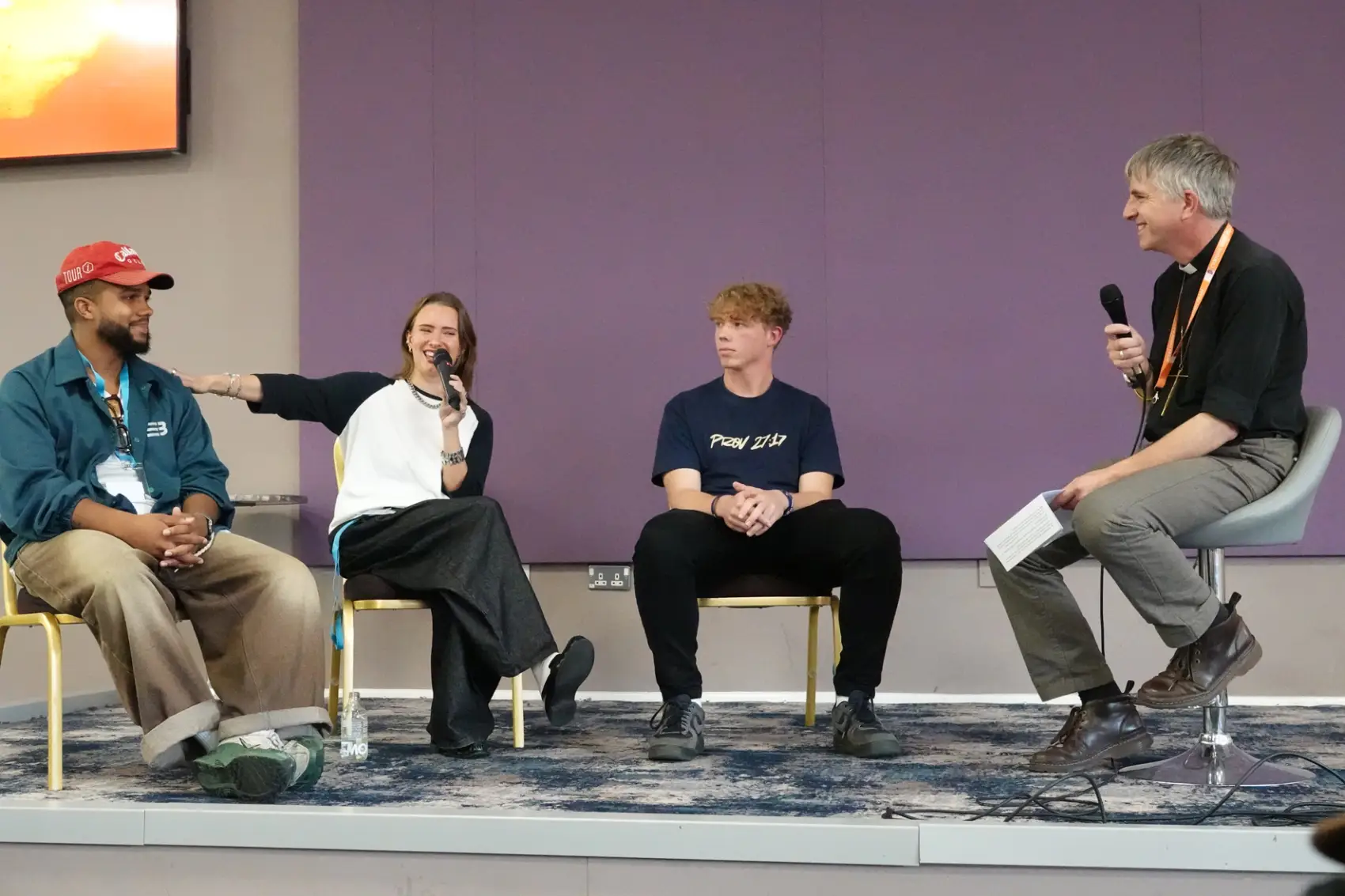 Three young people sat on a stage alongside Bishop Hugh as he interviews them.