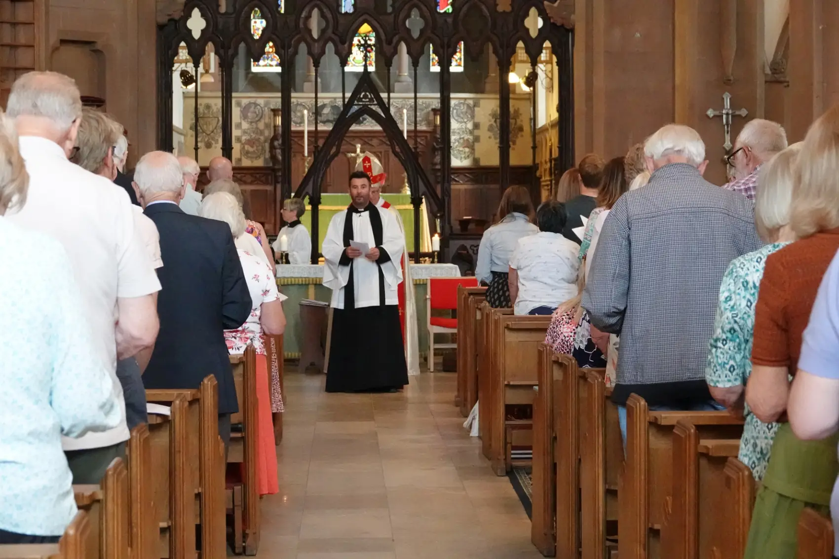 Chris Smith standing at the front of Pesnett church facing the congregation as they stand in the pews looking at him.