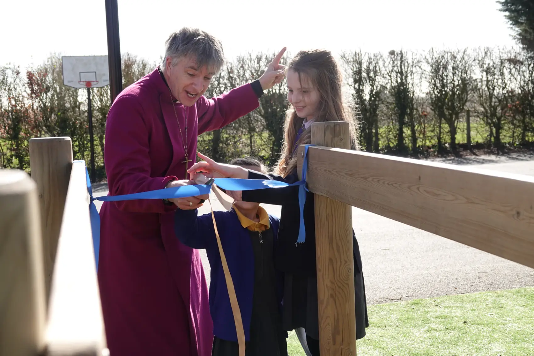 Bishop Hugh cuts a ribbon with the help of two students