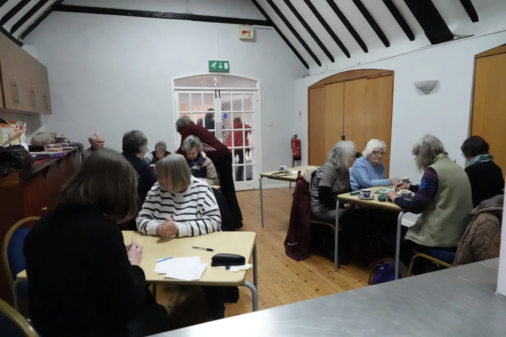 People in a room in a village hall sitting around tables playing games