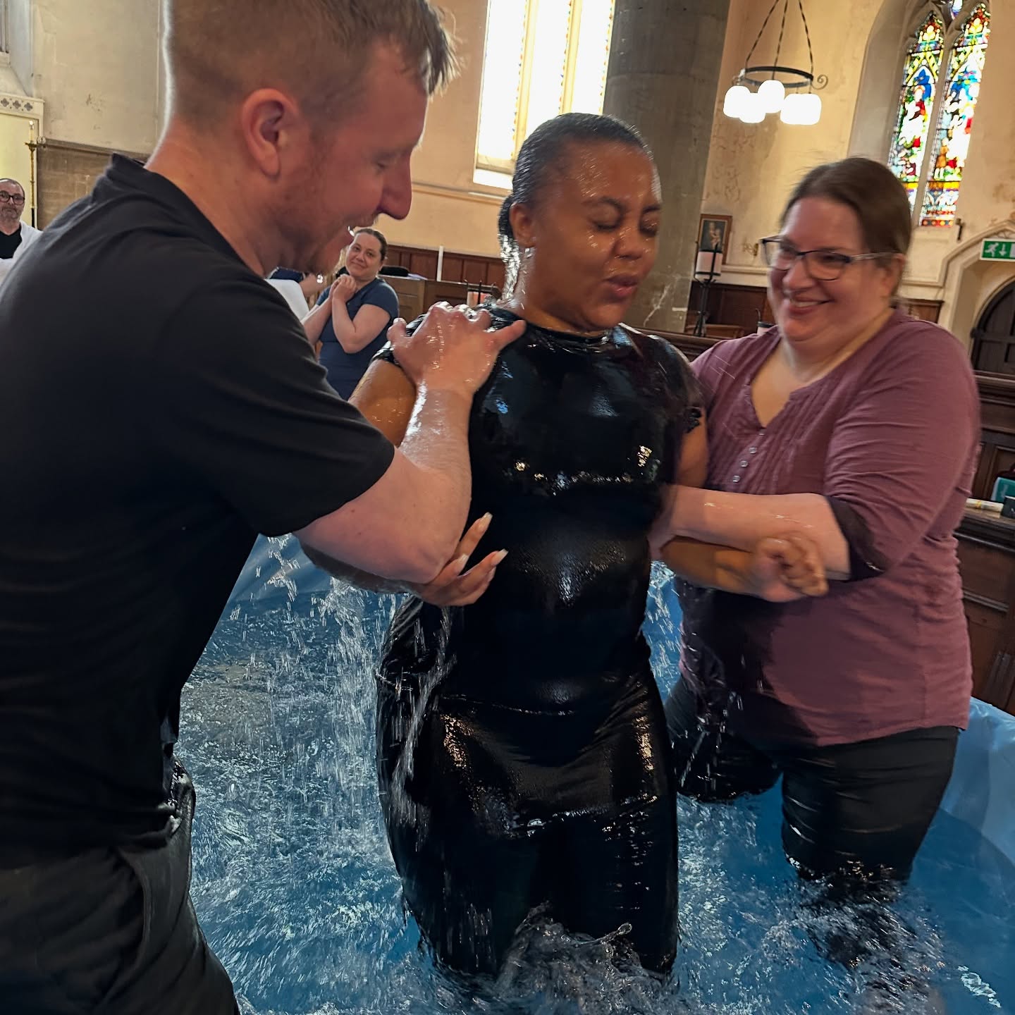 Girl having just had a full emersion baptism with a person either side pulling her up from the water