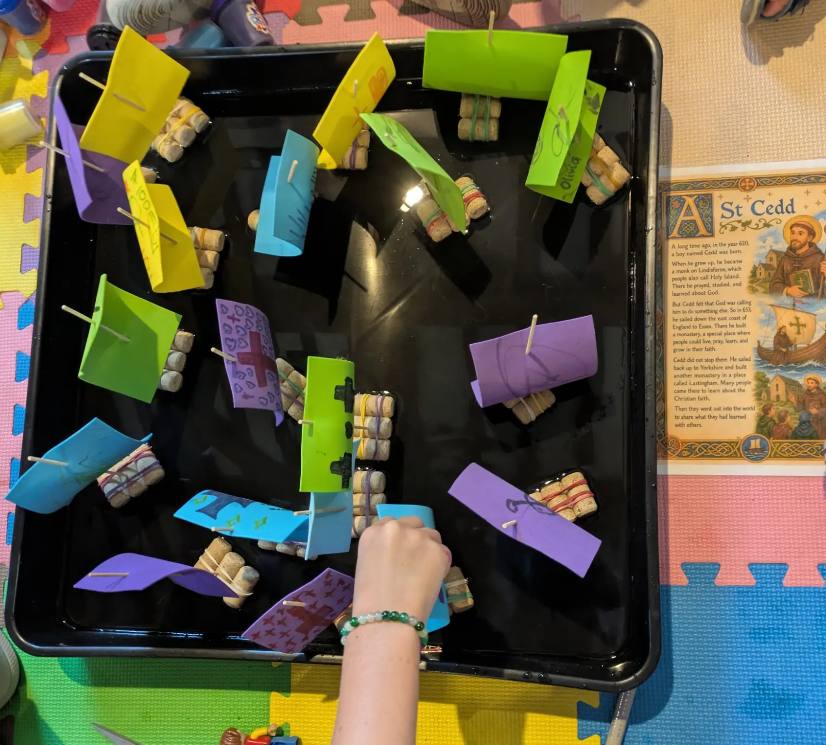 A tray with model boats with coloured paper sails and a hand moving one of the boats