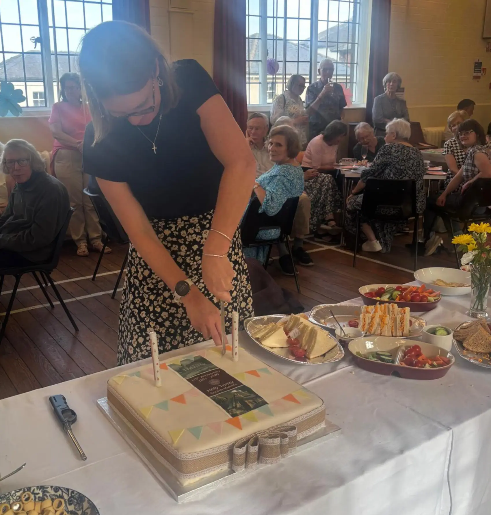 Becky Elliot cuts a cake for the 175 anniversary as people sit around tables behind her