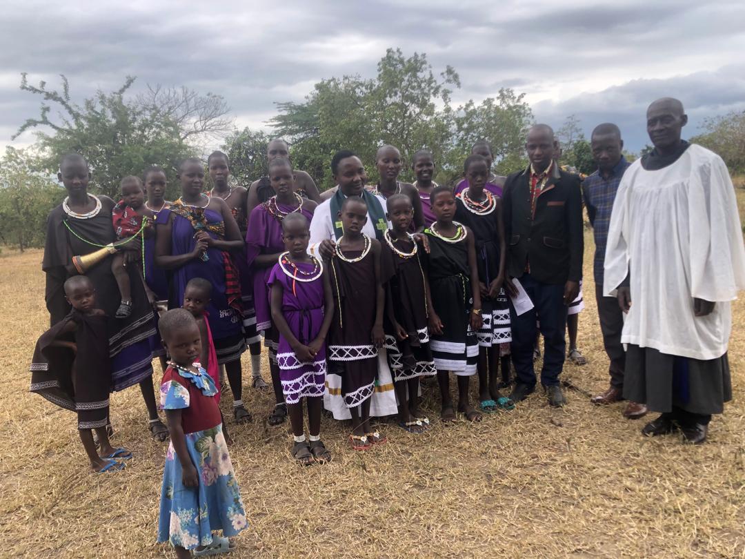 A group of Maasi people standing in a field next to a clergy person