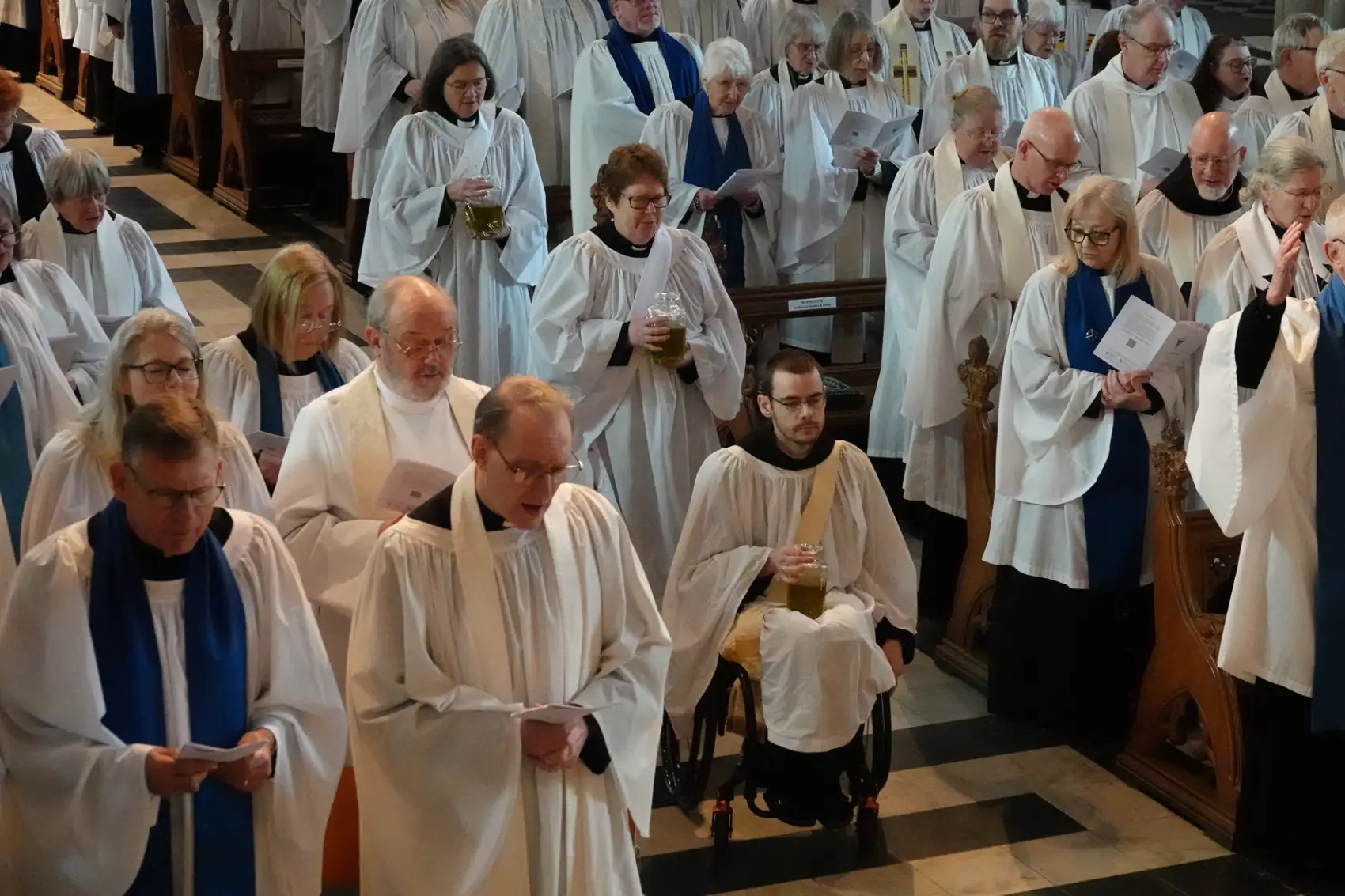 Three curates process down the aisle holding the oils to be blessed in the Chrism service