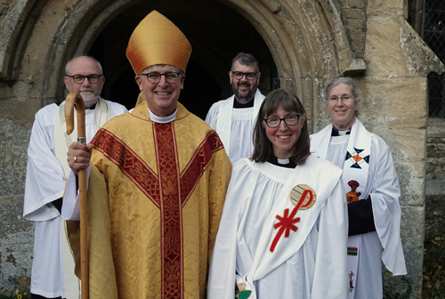 Elaine Simpson after her service of deaconing standing alongside Bishop Martin and some other clergy outside the door of Elmley castle church